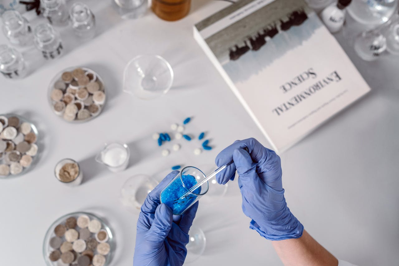 Top view of a scientist using a dropper with blue chemicals surrounded by laboratory equipment.
